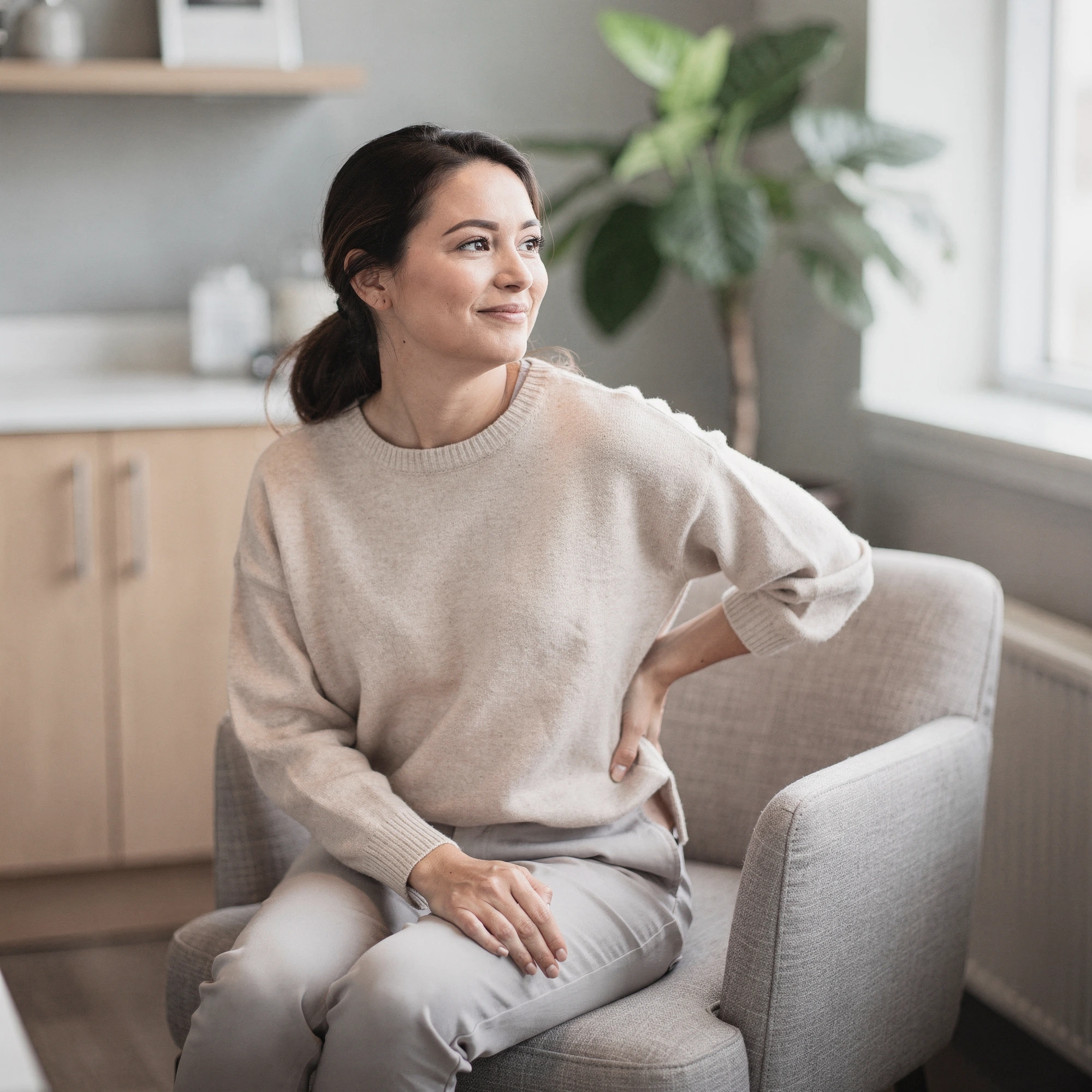 Woman sitting on a couch holding her lower back in discomfort